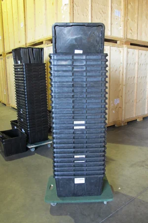 Stacks of black plastic moving bins on dollies in a warehouse
